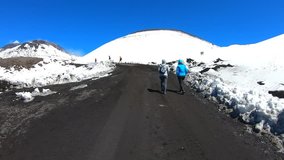 Fast motion time warp video of the tourists hiking on the top of Etna volcano taken on a sunny day. The volcanic path is surrounded by snow. Beautiful blue sky above. 