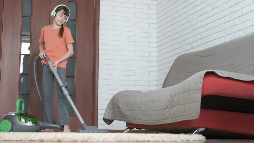 Child with a vacuum cleaner. Teen girl in headphones vacuuming the carpet.
