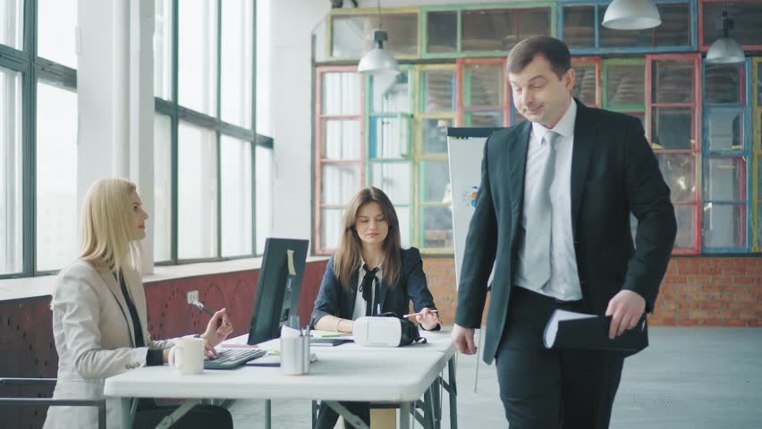 Businessman in a suit and with documents in hand walking in the office, talking and greeting with colleagues. Creative business space in loft style. Coworking. Office life | Shutterstock HD Video #1028825261