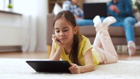 childhood, technology and family concept - little girl with tablet computer lying on floor at home