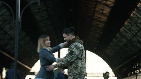 Happy Caucasian soldier throws his backpack to embrace his beloved girlfriend, wife, sister on a railway station. Army soldier returning home to the embrace of his wife. True love, happy reunion