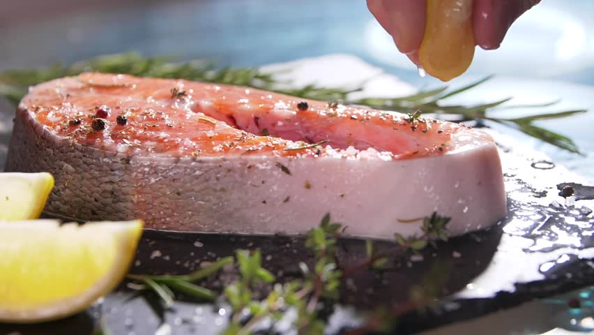 Slow motion close up view of unrecognizable hand squeezing lemon juice on salmon’s fillet. A chef's hand squeezes a fresh lime over a peace of sea fish. Mackerel in a marinade with spices Royalty-Free Stock Footage #1028829920
