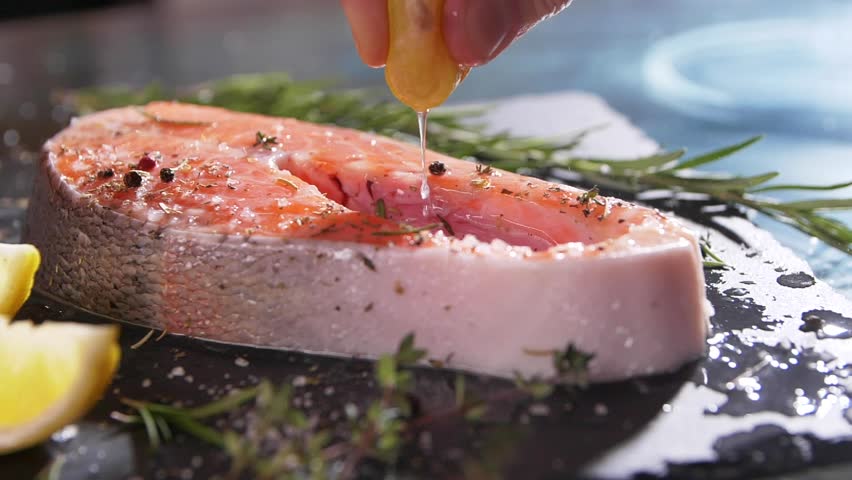 Slow motion close up view of unrecognizable hand squeezing lemon juice on salmon’s fillet. A chef's hand squeezes a fresh lime over a peace of sea fish. Mackerel in a marinade with spices