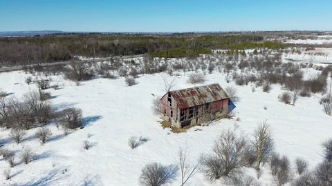 Static drone shot of an old red barn in a winter forest near Ottawa, Ontario.
