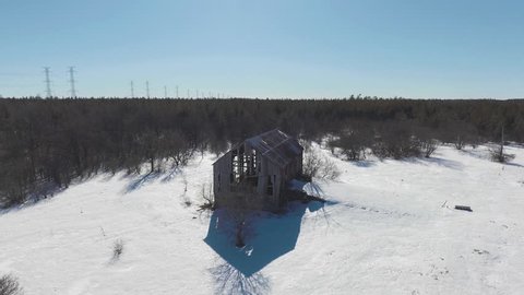 Drone footage towards an old red barn in a winter forest.