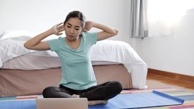 Young beautiful asian woman trying hard to learn yoga from internet using laptop in bedroom. Self learning from internet concept.