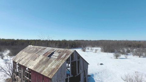 Rusty old red barn in sunny Canadian winter forest.