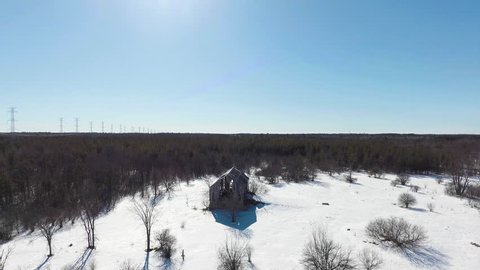 Dynamic drone shot of old barn in sunny winter forest.