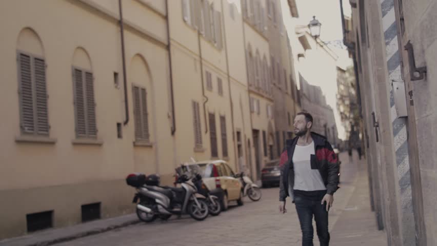 Cheerful young man in sport green and red jacket and black jeans walking in the summer European streets of Pisa