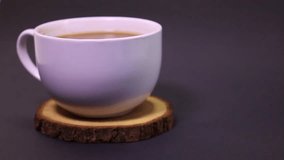 A white cup of bleached coffee placed on a wooden tray. Dark gray background.