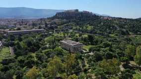Aerial bird's eye view video taken by drone of iconic Temple of Hephaestus in Ancient Agora and Acropolis hill at the background, Athens historic centre, Attica, Greece