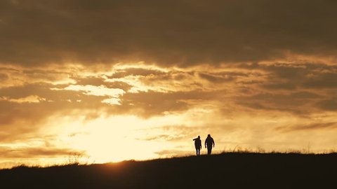 Silhouettes of two hikers with backpacks enjoying sunset view from top of a mountain. Enjoying the sunset view from mountain top above the clouds. Happy couple winner mountain top concept.