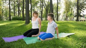 4k slow motion video of boy doing yoga exercises on grass at park with his mother. Woman teaching child in fitness class