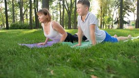4k slow motion video of adult woman teaching teenage boy yoga in park. Fitness class exercising in nature
