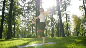 4k slow motion video of mid aged smiling woman practicing yoga in the public park at sunny summer day. Concept of body and mental health