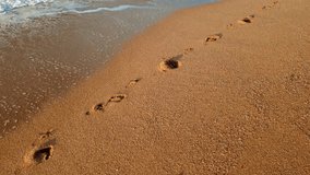 4k video of camera flying above the footprints on the wet sand at sea beach