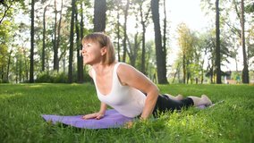 4k video of middle aged woman exercising in park. Adult female practising yoga on fitnes mat at forest