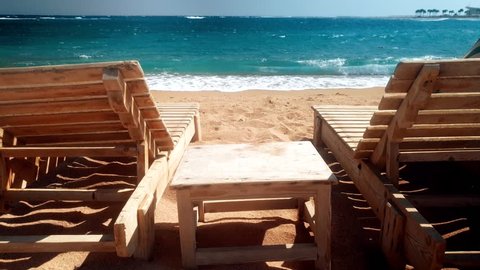 4k footage of two wooden sunbeds on the beach. High waves rolling over the coast