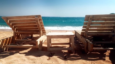 4k footage of two wooden sunbeds and small table on the abandoned sea beach