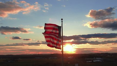 Flag of the United States in dramatic sunset,ing across the frame in front of the sun, waving in the wind, 4k UHD