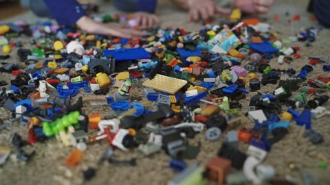 VINNITSA, UKRAINE - APRIL 2019: Unrecognizable hands throwing many lego blocks on the floor in the room. A lot of small colorful lego bricks in a mess lying on the carpet.