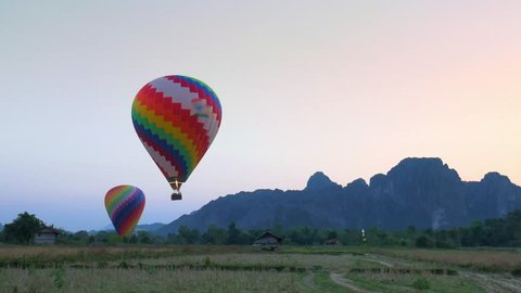 Hot air balloons landing in Vang Vieng backpacker travel destination in Laos, Asia. Tourist activity scenic cliffs rock pinnacles sunset landscape.