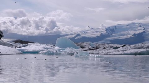 Iceland Travel - EPIC landscape shot of Iceland Glaciers with Seagulls and Seals in a Crystalline lake with Clouds and Snow-capped Mountains in the Background