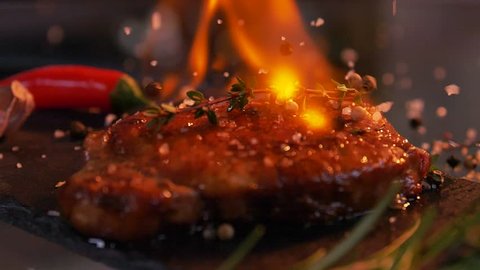 Slow-motion footage of throwing salt and pepper on fresh beef meat on ignited pan.
