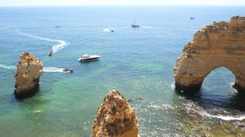 Multiple ships and boats and kayaks between the natural arc and cliffs of Praia da Marinha in Portugal