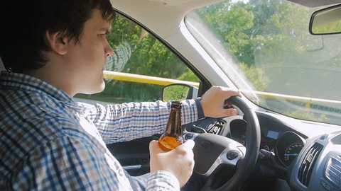 Slow motion footage of irresponsible man driving car and drinking alcohol beer.
