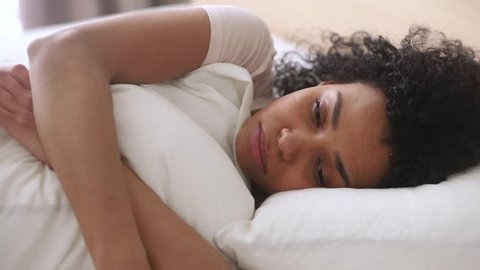 Depressed upset african american woman feeling sad lonely lying in bed alone trying to sleep thinking of problem, frustrated mixed race black girl suffer from anxiety and insomnia in bedroom