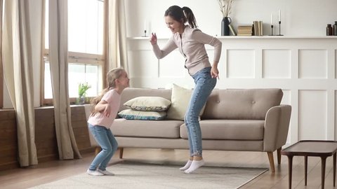 Happy family young mom babysitter having fun with cute little kid girl dancing in living room, carefree mother with child daughter laughing jumping enjoying funny activity playing together at home