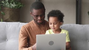Happy black father teach cute kid son learn to read use laptop at home for children education, smiling caring african dad and little child boy looking at computer screen do online shopping at home