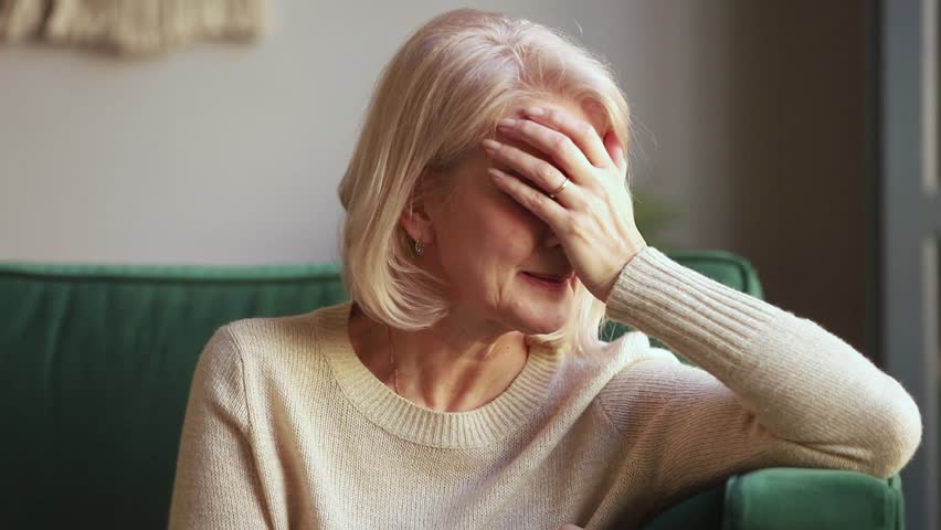 Desperate sad grieving old widow crying covering face with hands sitting on sofa alone, upset miserable middle aged mature woman in tears feeling sorrow suffer from loneliness mourning, grief concept Royalty-Free Stock Footage #1028900150