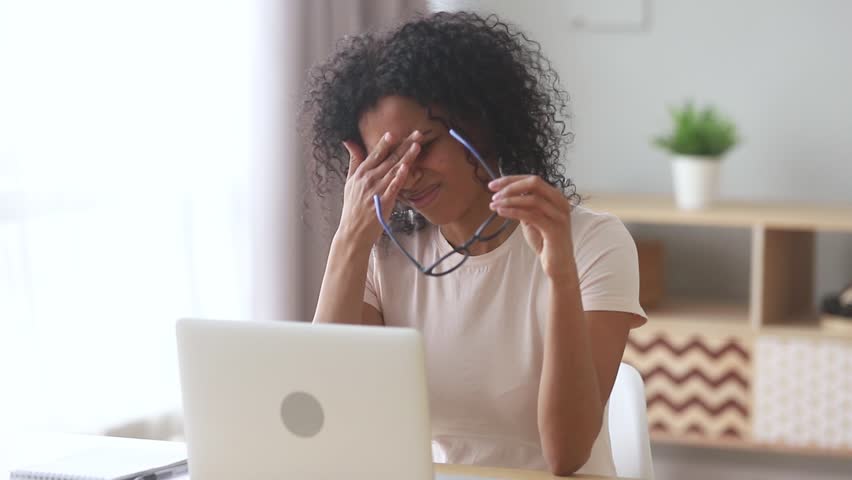 Tired overworked young african woman feel fatigue eye strain headache after computer work take off glasses, stressed mixed race female student suffer from pain in dry eyes, bad vision sight problem  | Shutterstock HD Video #1028900189