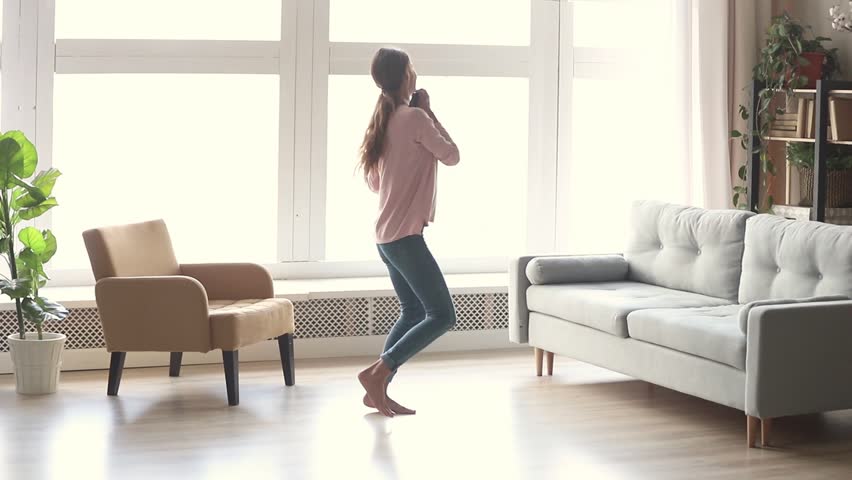 Happy carefree young woman dancing alone in modern living room with big window listen to music on smartphone, funky millennial girl holding phone enjoy new hit song playing in app having fun at home Royalty-Free Stock Footage #1028900228