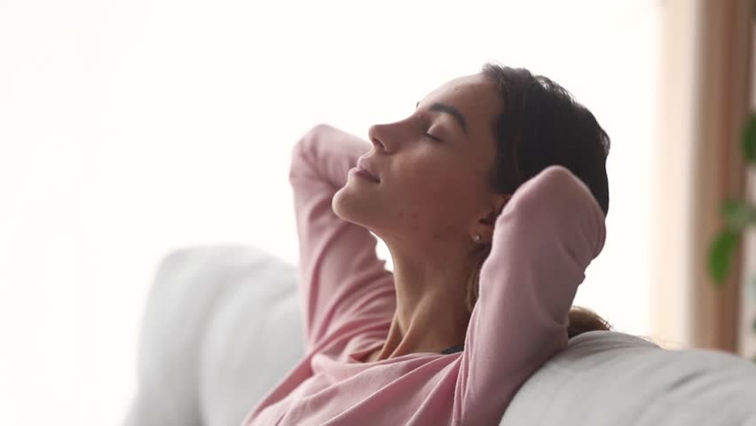 Calm young woman relax with eyes closed take deep breath of fresh air dream nap on couch, healthy girl rest on sofa enjoy meditation do yoga exercises feel stress relief peace of mind lounge at home Royalty-Free Stock Footage #1028900258