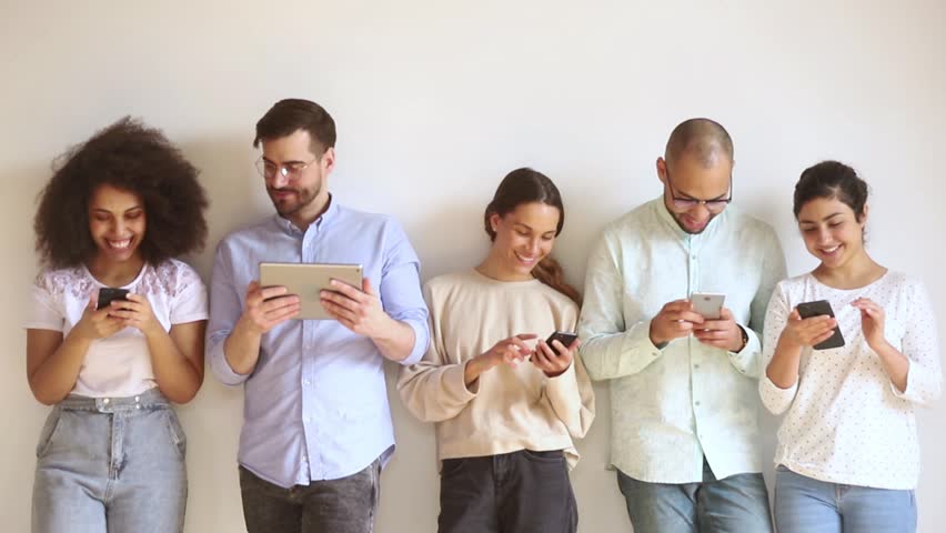 Multiracial smiling young people group using gadgets stand in row against wall, happy diverse female male users obsessed with modern technology devices holding phones tablet, tech addiction concept Royalty-Free Stock Footage #1028900291