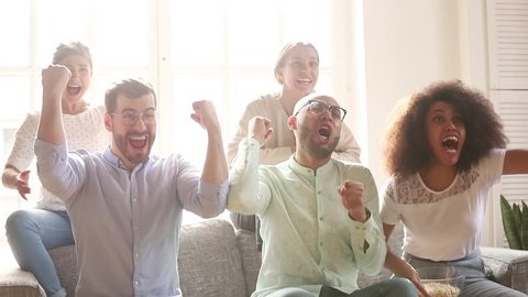 Overjoyed multicultural friends group football fans watching sport tv game sit on couch together, diverse happy people excited by goal score scream celebrate victory support cheering winning team
