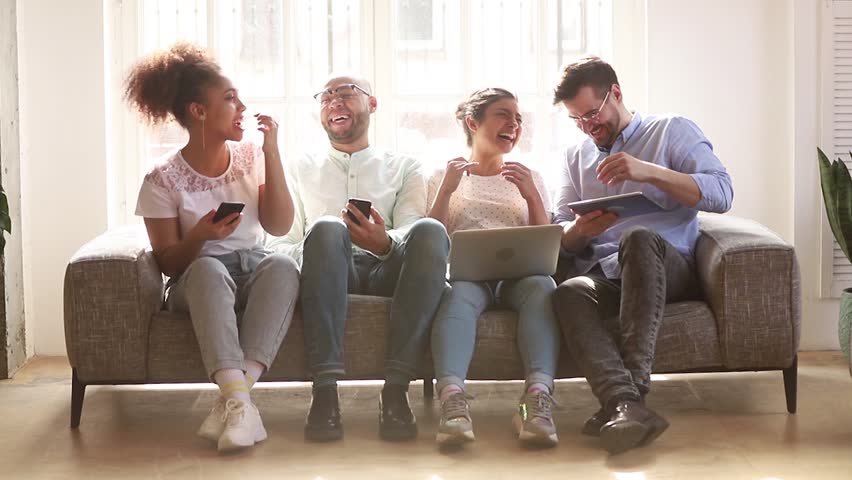 Happy diverse friends group using devices phones laptop digital tablet sit on sofa indoor, cheerful multicultural young people students laughing talking having fun with gadgets technology together Royalty-Free Stock Footage #1028900306