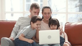 Happy family of four mom dad and little children having fun with laptop looking at screen sit on sofa together, parents teaching kids using computer apps online enjoy spend time with device at home 