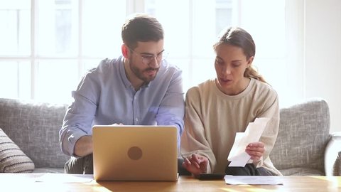 Serious millennial couple calculating domestic paper bills at home with laptop computer paying online, focused family man and woman planning budget, managing bank loan payments, household economy