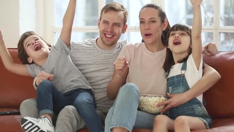 Excited family football fans watching sport tv game celebrating goal together, happy parents mom dad and little kids children with snack supporting favorite soccer team victory at home sit on sofa