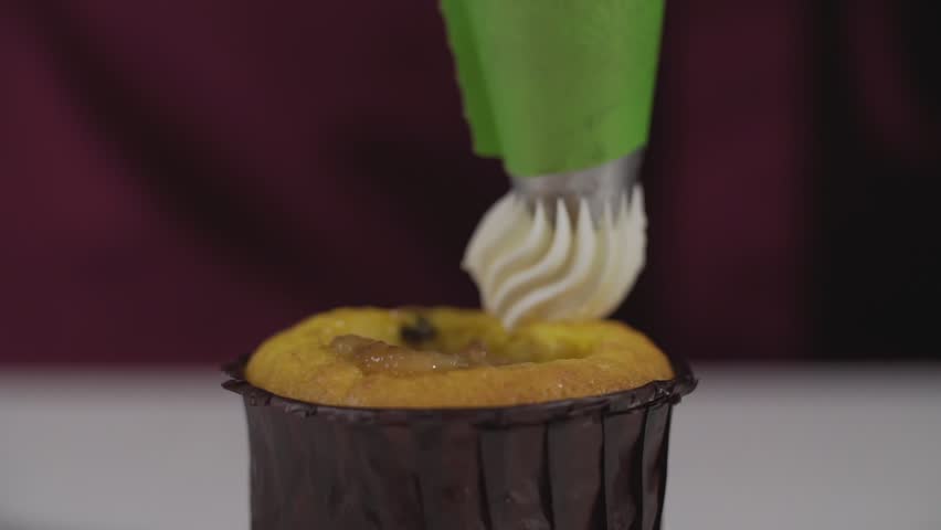 Decorating cup-cake with cream. Using cooking bag, confectioner making desserts for party. Shot of woman