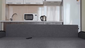 A man siting on the sofa and switches channels on the TV. A yuong guy taking a remote control and in a hurry looking for the right channel for him. The kitchen on background. 4K footage.