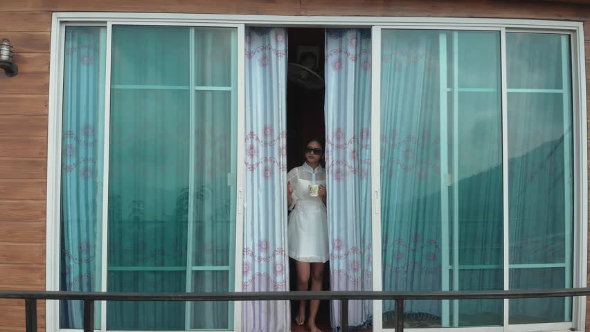 Attractive asian girl in white dress walk on balcony with cup of drink to enjoy mountain valley view from the House on the Hill