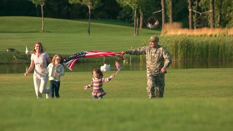 Running with big USA background in the park. Soldier in holding huge flag with his wife and moving, slow motion.