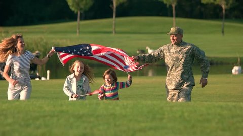 USA family with backgrounds coming up, front view. Military man with his wife with daughters running to the camera.