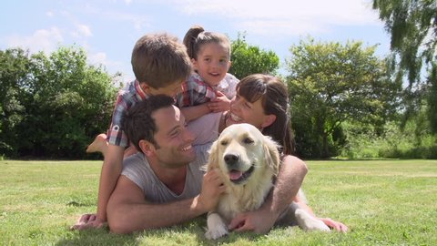 Family piled up on grass in garden with pet golden retriever.Shot on Sony FS700 at frame rate of 25fps