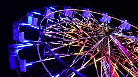 brightly lit ferris wheel ride spinning at night at a carnival, amusement park, theme park, fair, thrill park.